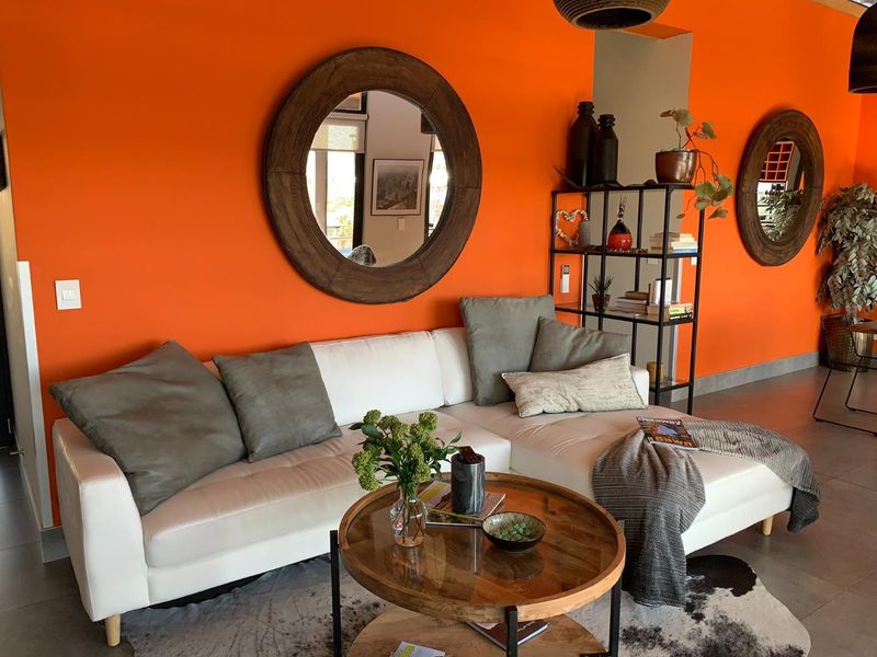 A vibrant living room featuring bright orange walls, tiled flooring, and modern architectural finishes, providing a bold and contemporary space for relaxation.