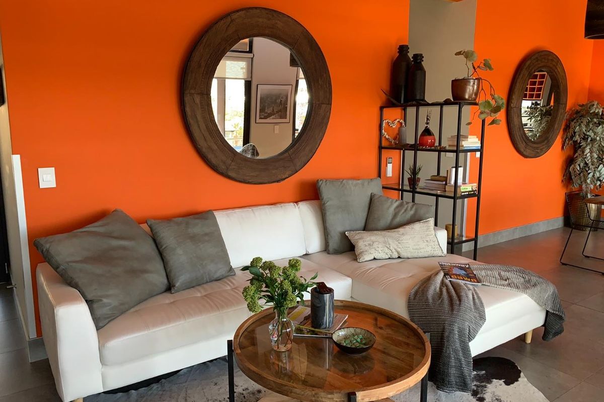 A vibrant living room featuring bright orange walls, tiled flooring, and modern architectural finishes, providing a bold and contemporary space for relaxation.