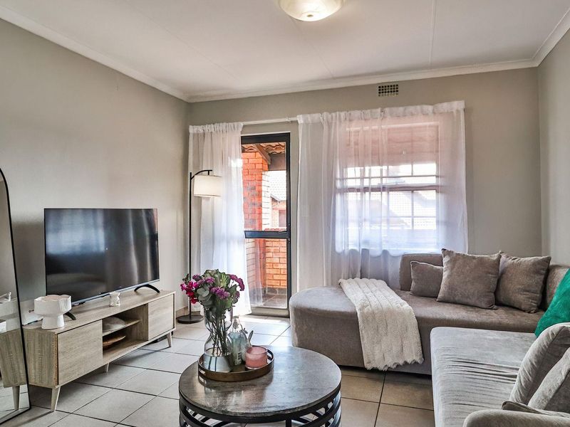 A comfortable living room featuring tiled flooring, neutral wall tones, and direct access to an outdoor balcony area through a sliding glass door.