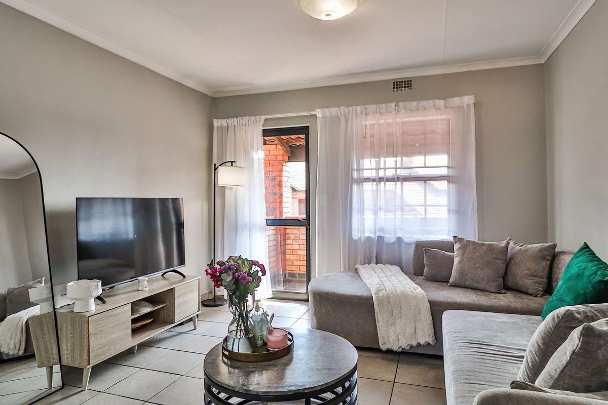 A comfortable living room featuring tiled flooring, neutral wall tones, and direct access to an outdoor balcony area through a sliding glass door.