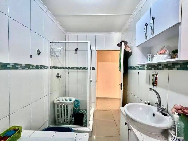A functional bathroom featuring a glass shower enclosure, a vanity unit with a basin, and wall-mounted storage cabinetry with tiled finishes throughout.
