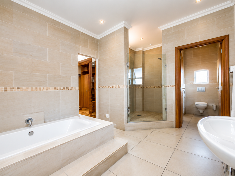 Spacious modern bathroom featuring a built-in bathtub, separate glass shower enclosure, and a private toilet area with neutral floor-to-ceiling tiling.
