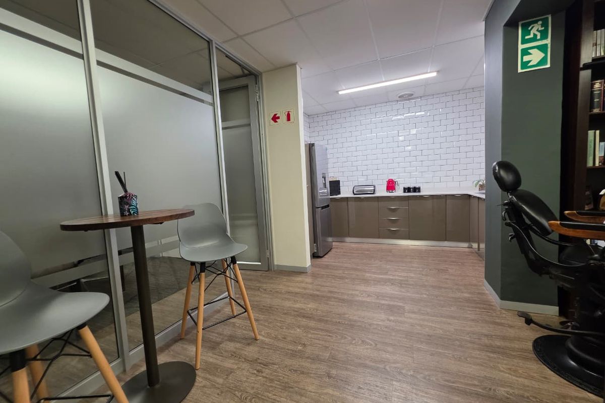 A modern office kitchenette featuring sleek cabinetry, a white subway tile backsplash, and durable laminate flooring, adjacent to a glass-partitioned workspace.