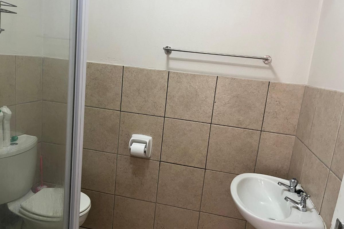 A functional bathroom featuring a pedestal basin, a toilet, and a glass-enclosed shower with neutral wall tiling.