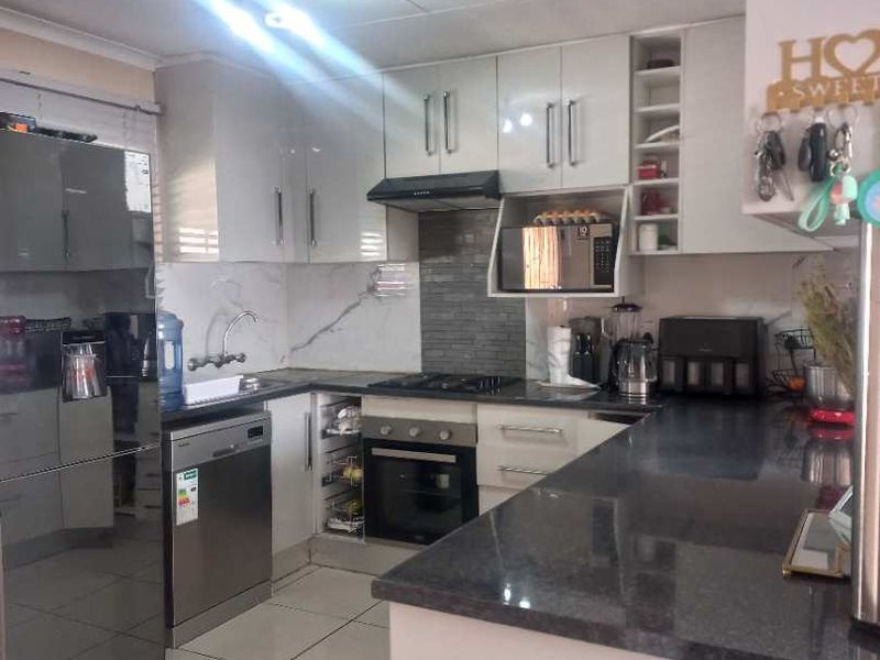 Modern kitchen featuring high-gloss cabinetry, granite countertops, built-in oven, gas hob, extractor fan, and integrated dishwasher with tiled flooring.