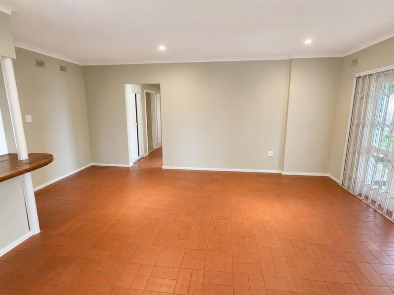 A spacious, empty living area featuring terracotta tile flooring, recessed lighting, and a sliding glass door with a security gate leading outdoors.