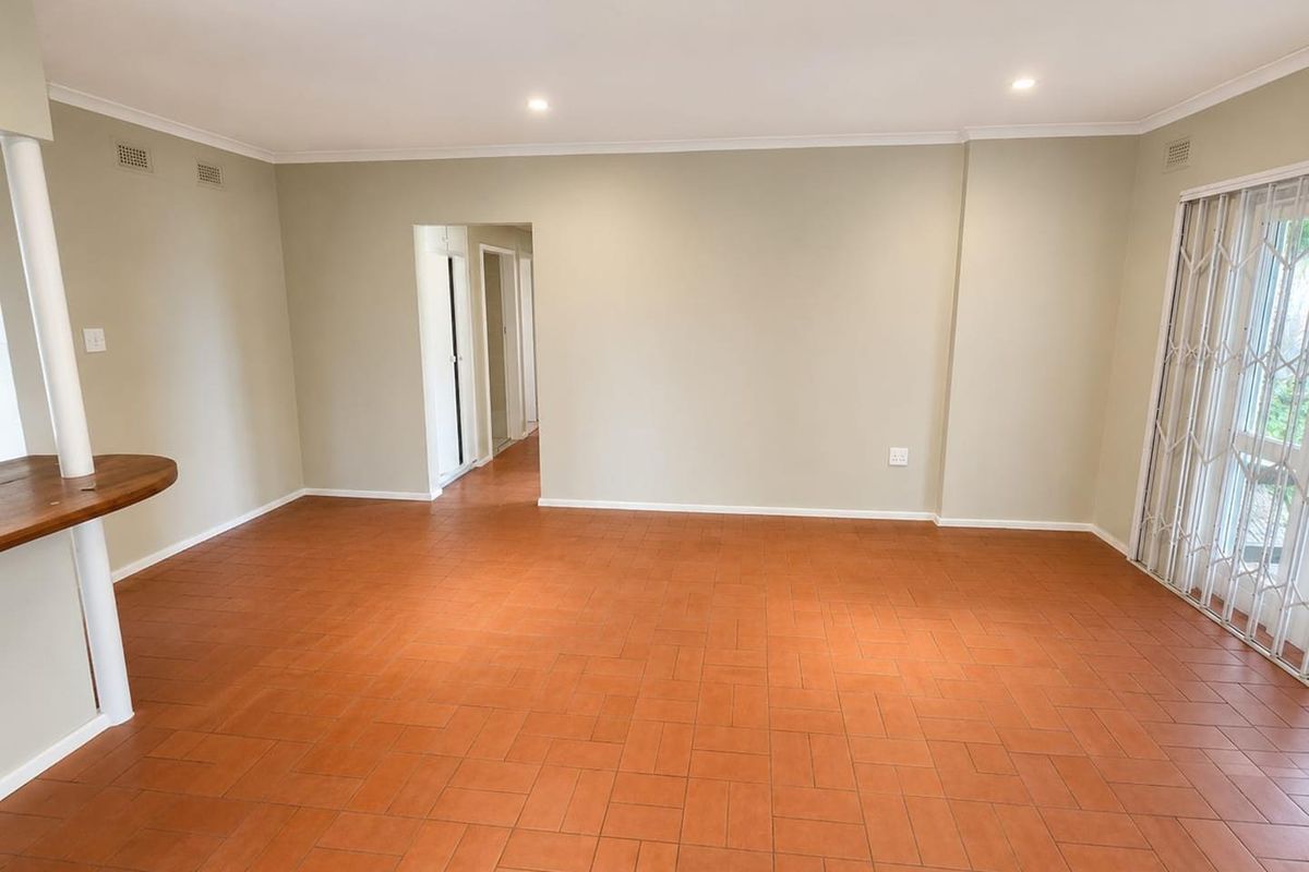 A spacious, empty living area featuring terracotta tile flooring, recessed lighting, and a sliding glass door with a security gate leading outdoors.