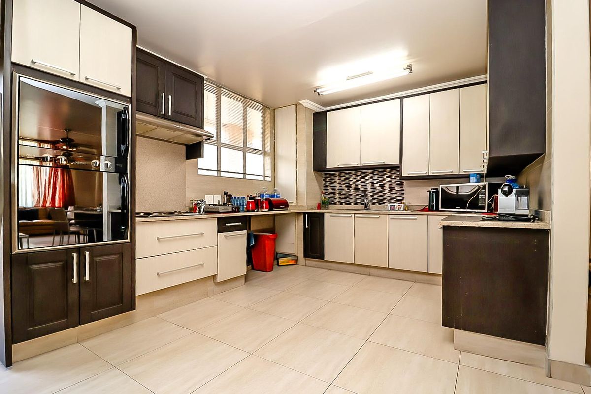 Modern kitchen featuring two-tone cabinetry, stone countertops, integrated oven, extractor fan, and tiled backsplash with ample storage space.