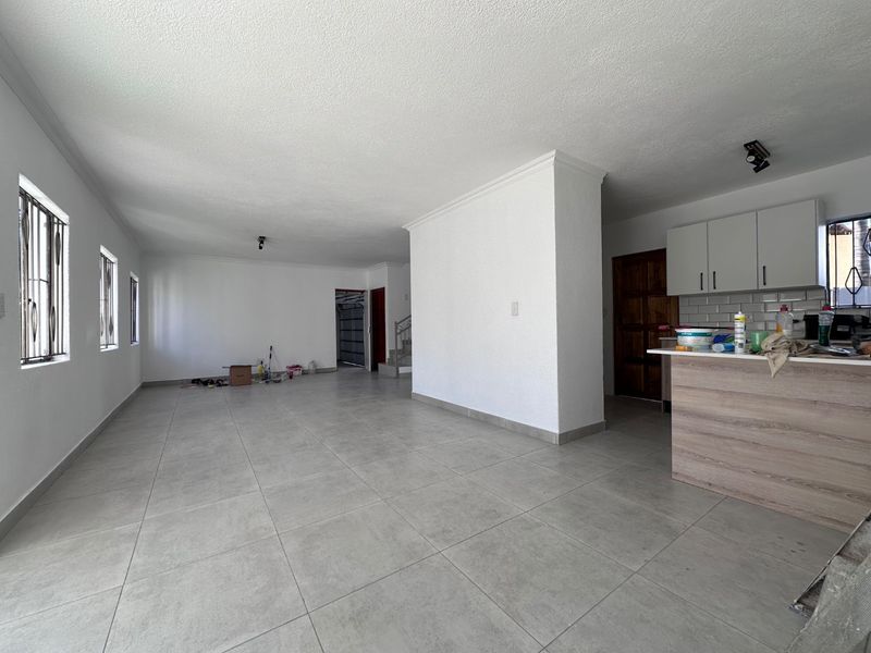Spacious open-plan living area featuring large format floor tiles, a modern kitchen island with cabinetry, and a neutral finish throughout.