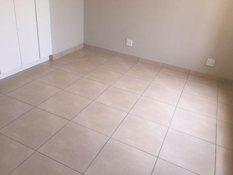 A clean, empty bedroom featuring neutral tiled flooring and built-in cupboards, providing a versatile blank canvas for personalization.