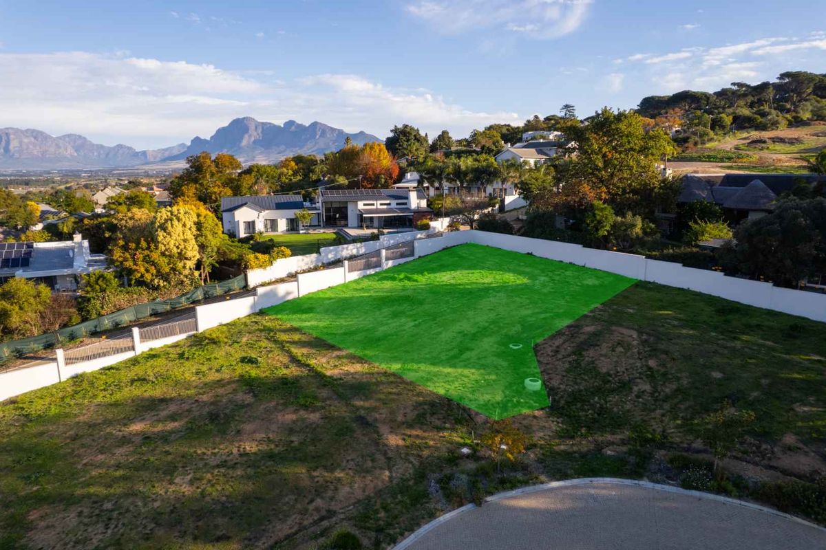 Aerial view of a vacant residential plot featuring boundary walls and surrounding neighborhood context with mountain views.
