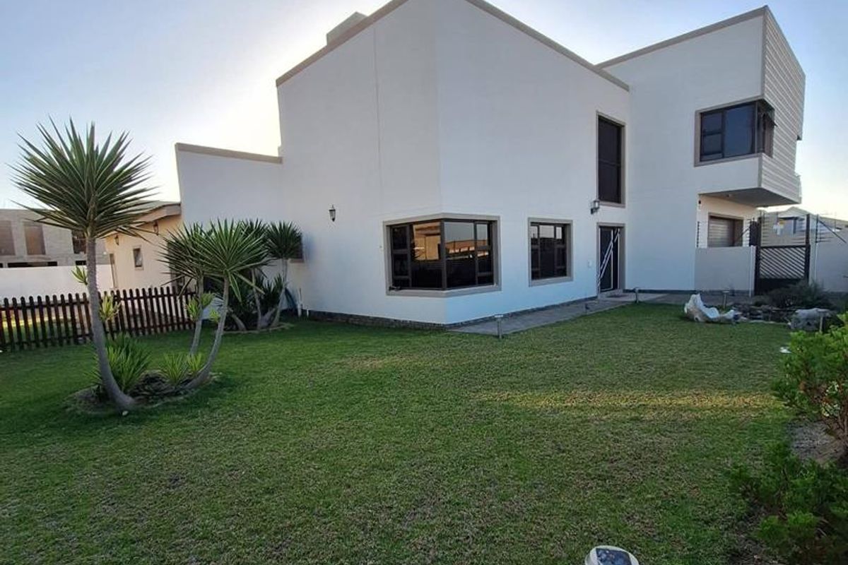 A view of the rear exterior of a modern two-story house featuring a well-maintained lawn and landscaped garden area.