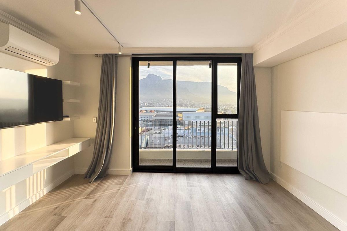 Bright, modern living area featuring laminate flooring, track lighting, air conditioning, and a sliding door leading to a balcony with mountain views.