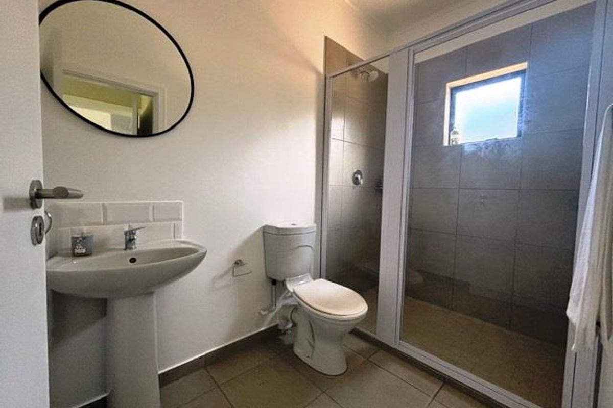 A modern bathroom featuring a pedestal basin, a close-coupled toilet, and a walk-in shower with a glass enclosure and tiled walls.