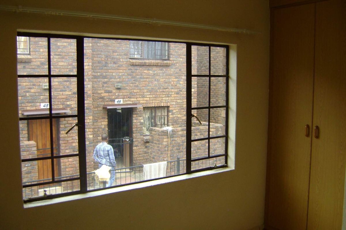 A bedroom interior featuring built-in wooden cupboards and a steel-framed window overlooking an exterior brick courtyard.