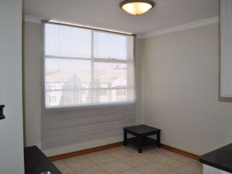 A bright, neutral-toned kitchen area featuring tiled flooring, crown molding, and a large window with fitted blinds, offering a clean and functional space.