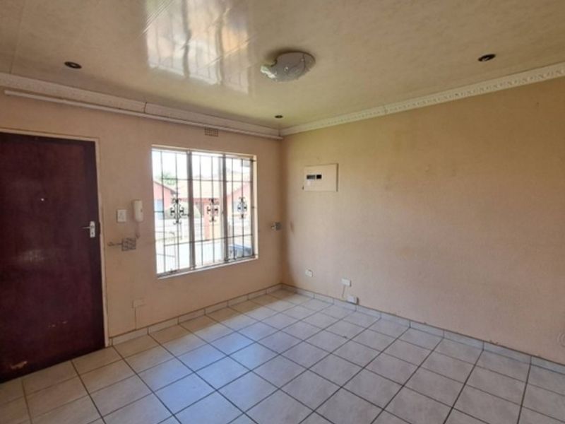 An empty living room featuring tiled flooring, security bars on the window, and recessed ceiling lighting, offering a blank canvas for renovation.
