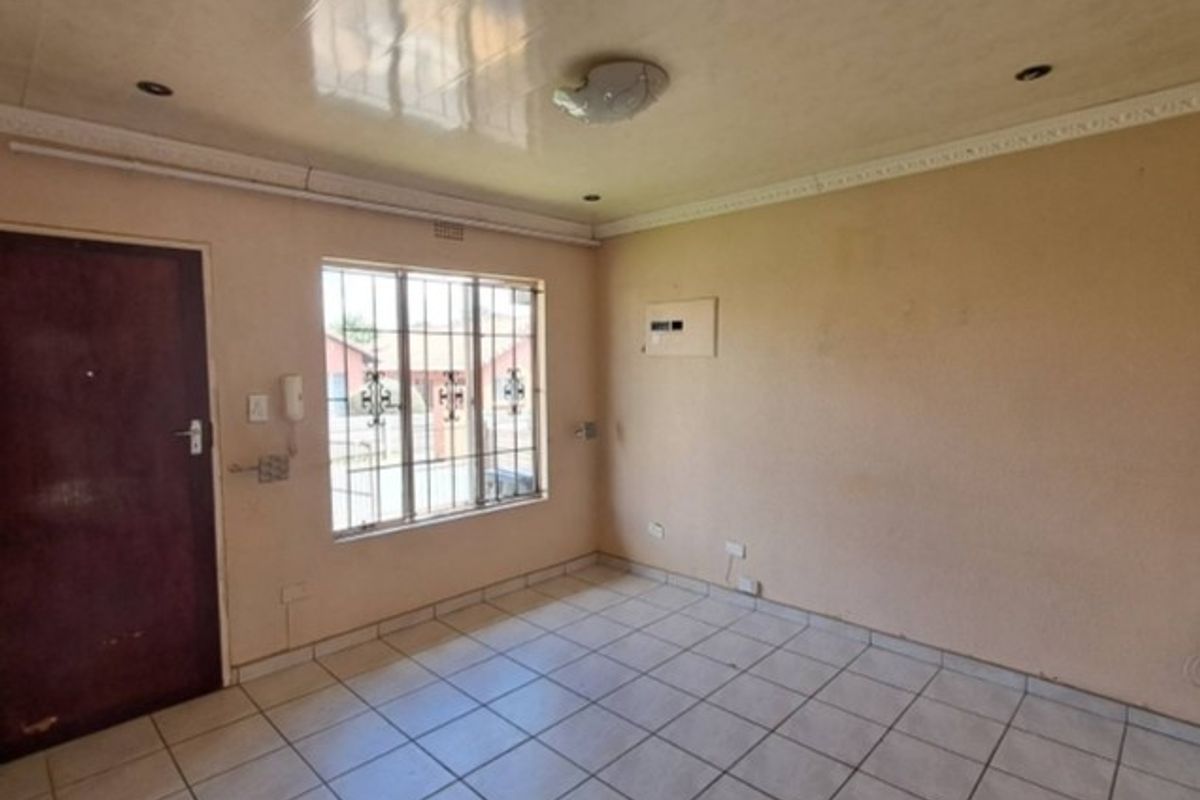 An empty living room featuring tiled flooring, security bars on the window, and recessed ceiling lighting, offering a blank canvas for renovation.