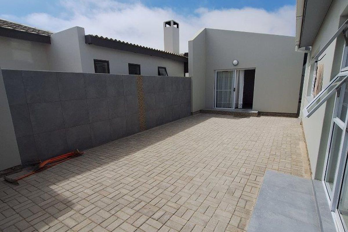 A paved rear courtyard area featuring a decorative tiled boundary wall and direct access to the main dwelling through sliding glass doors.
