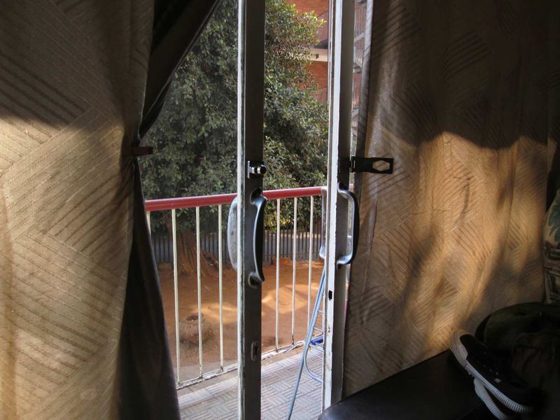 A view from an interior room looking out through a sliding glass door onto a small balcony with a metal balustrade.