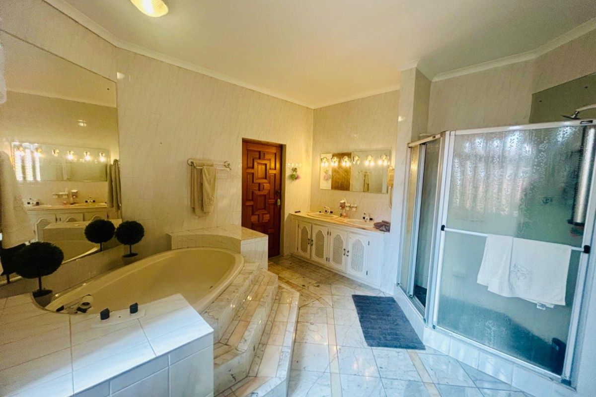 Spacious bathroom featuring a built-in sunken bathtub with tiled surround, a double vanity with integrated sinks, and a separate glass-enclosed shower.