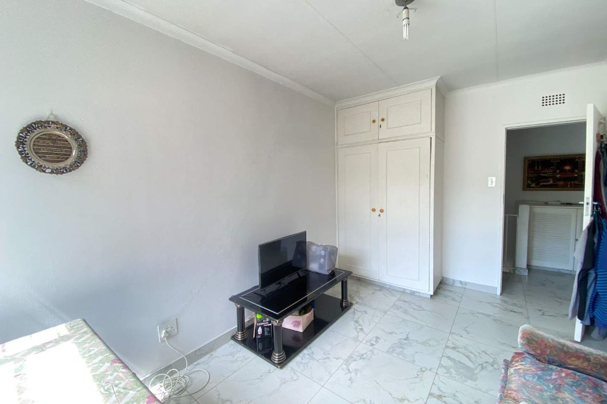 A bedroom featuring white tiled flooring, a built-in wardrobe with overhead storage, and a standard ceiling light fixture.