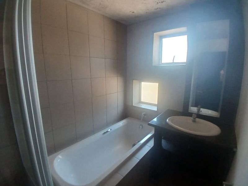 A compact bathroom featuring a built-in bathtub, vanity cabinet with integrated sink, and tiled wall finishes, requiring some ceiling maintenance.