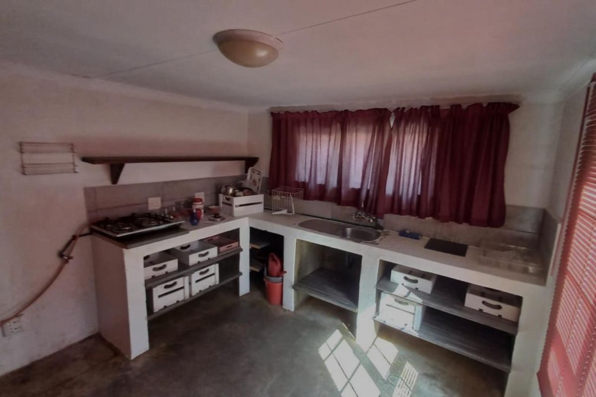 A functional kitchen area featuring built-in concrete cabinetry, a stainless steel sink, and a gas hob with open shelving and tiled splashback.