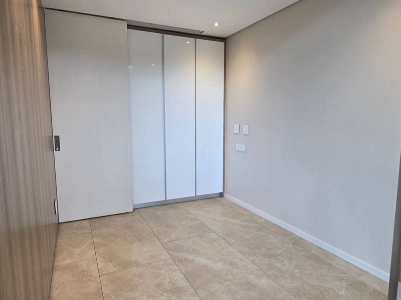 A modern, empty bedroom featuring neutral tiled flooring, built-in white cabinetry, and recessed ceiling lighting.