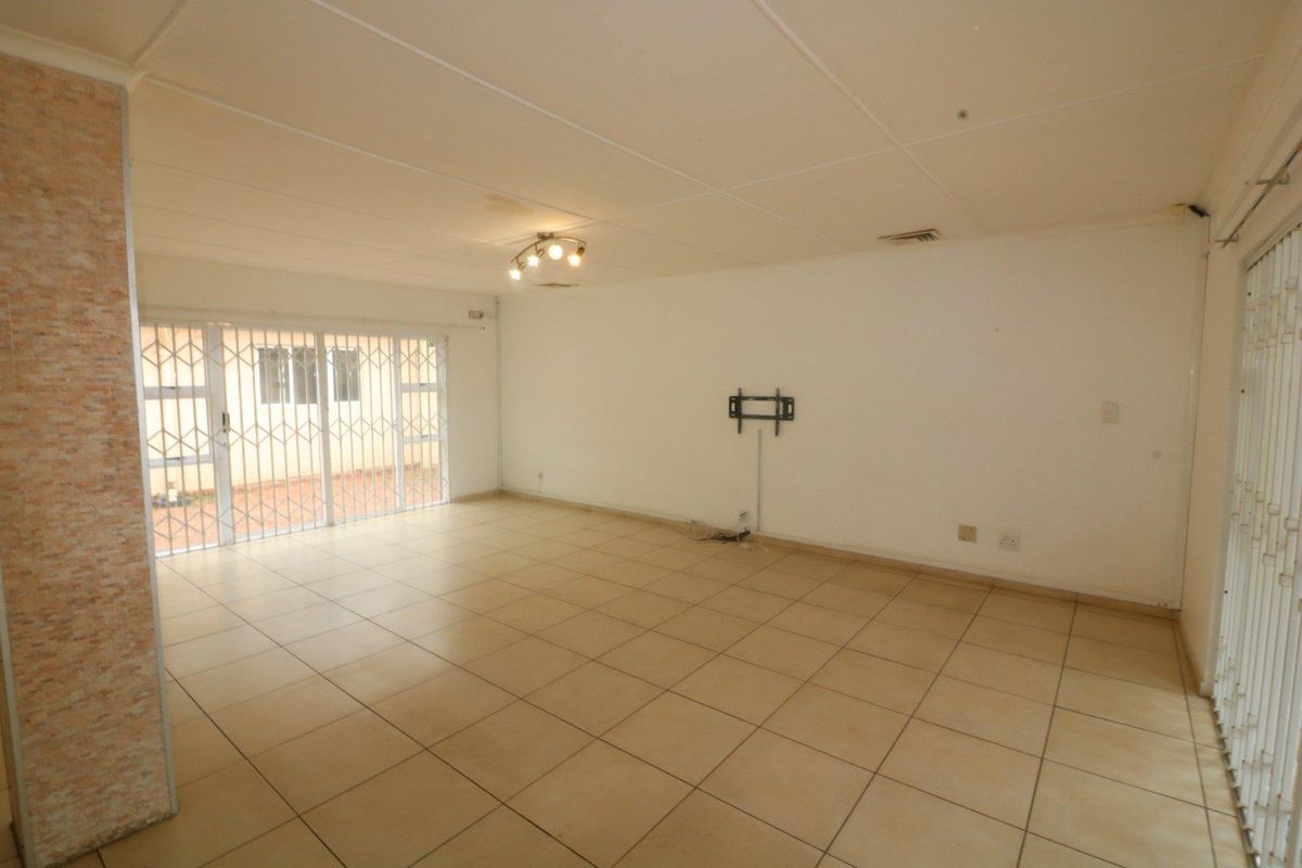 A spacious, empty living area featuring neutral tiled flooring, security gates on sliding doors, and a wall-mounted TV bracket.