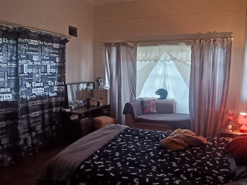 A bedroom featuring a window with curtains and a built-in wall ventilation vent.