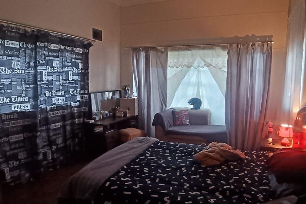 A bedroom featuring a window with curtains and a built-in wall ventilation vent.