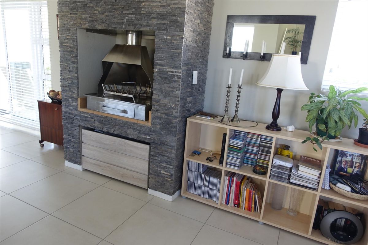 Living area featuring a prominent stone-clad built-in fireplace with a stainless steel braai insert and neutral tiled flooring.