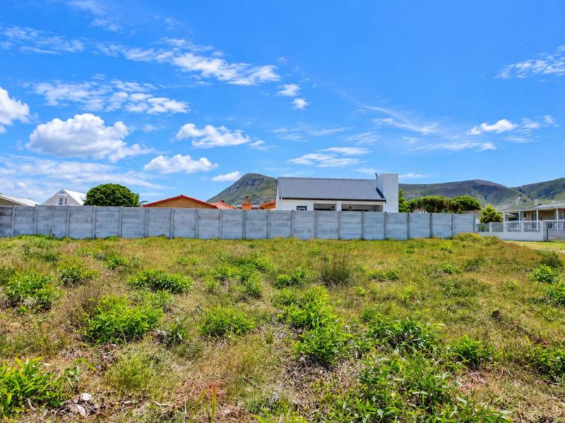 A vacant residential plot featuring natural vegetation and a precast concrete boundary wall, set against a scenic mountain backdrop.