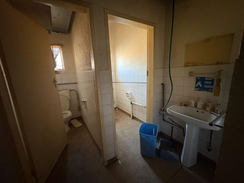 A dated bathroom featuring a pedestal basin, toilet, and tiled walls, requiring significant renovation and modernization of fixtures and finishes.