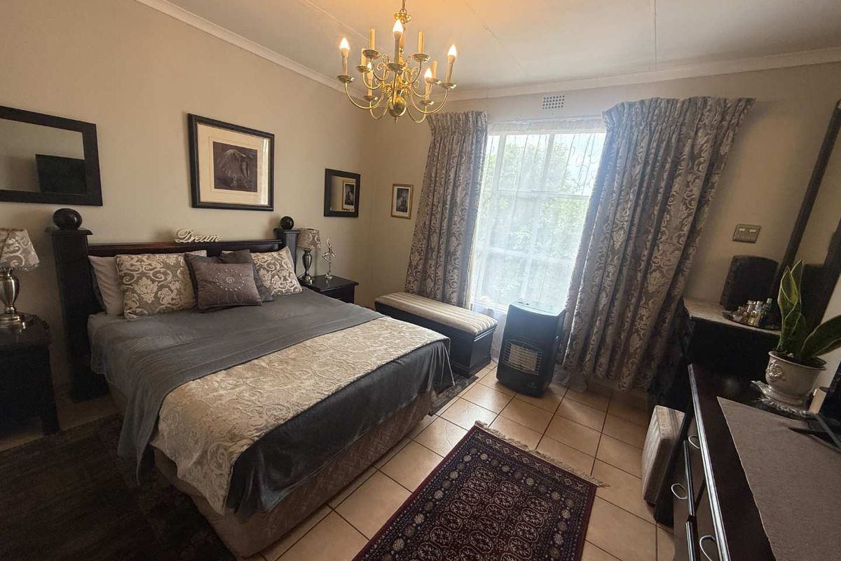 A well-proportioned bedroom featuring tiled flooring, a central chandelier, and a large window with curtain treatments, offering a functional and comfortable living space.