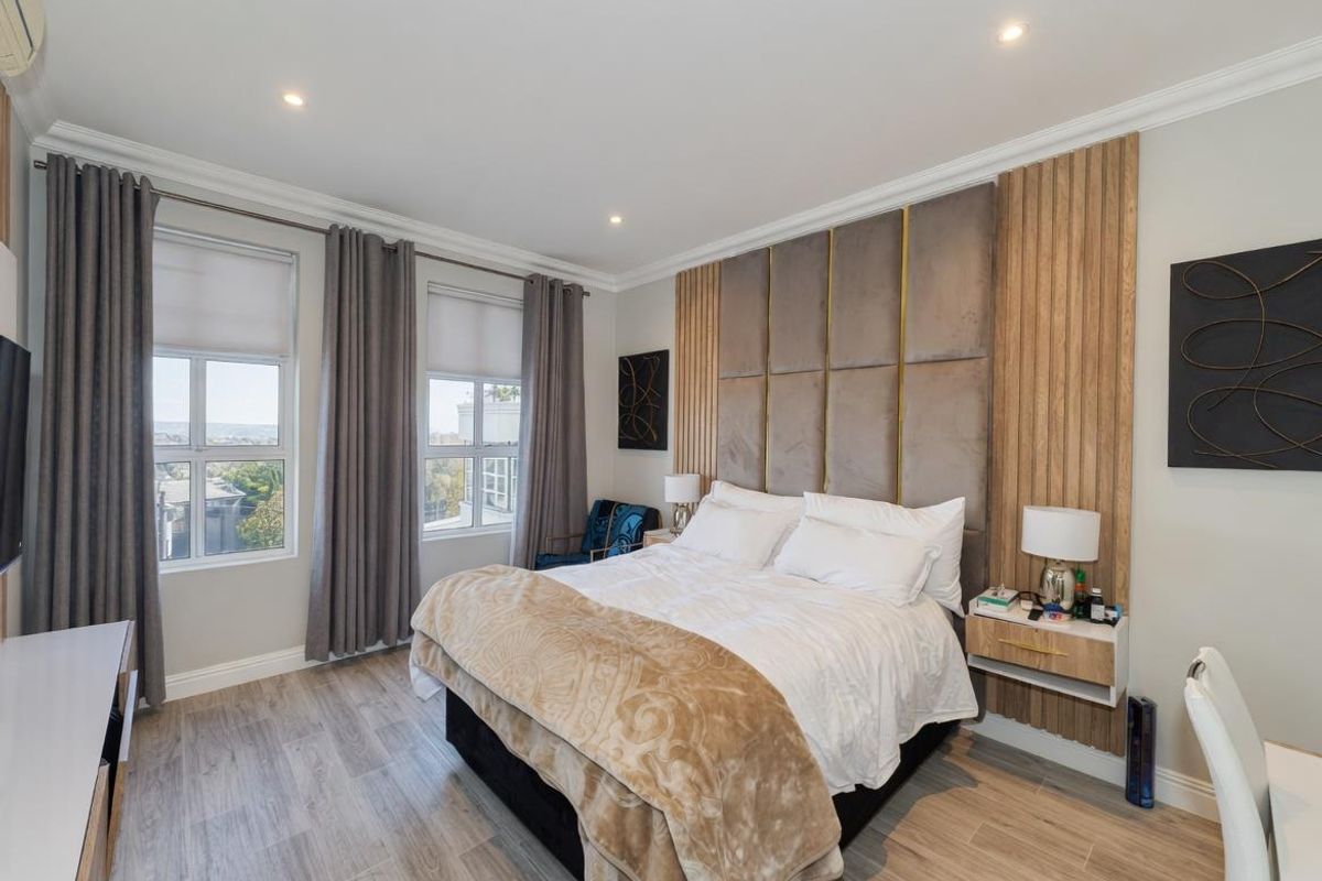 A well-appointed bedroom featuring a custom upholstered headboard with integrated wood paneling, recessed downlighting, and wood-look flooring.
