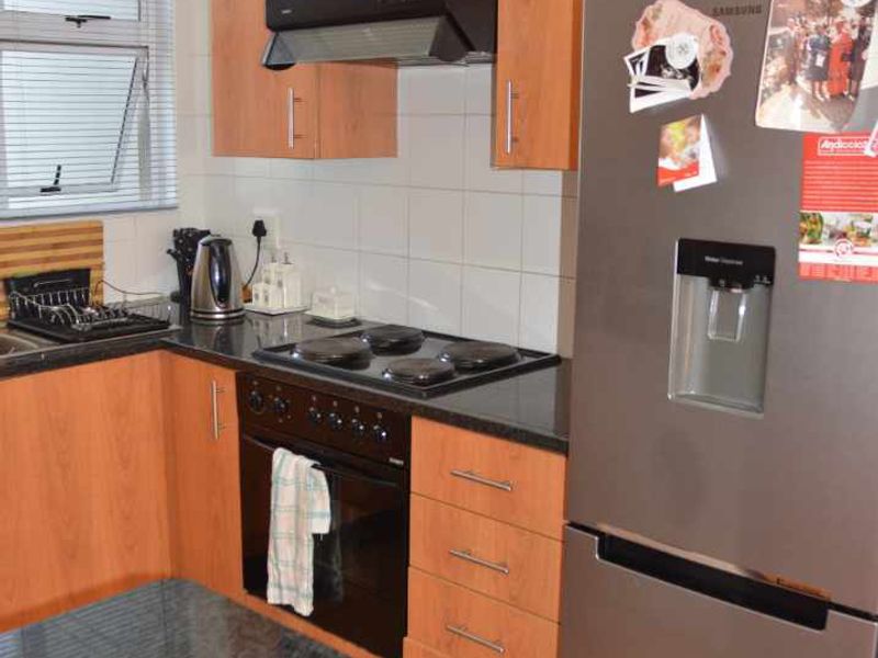 A functional kitchen featuring laminate cabinetry, granite countertops, built-in oven, electric hob, and tiled backsplash with neutral floor tiles.