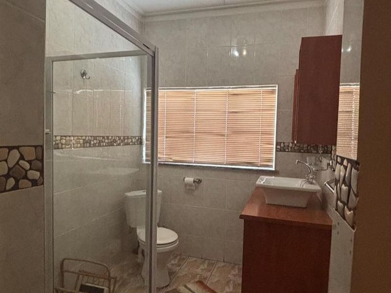 A functional bathroom featuring a glass-enclosed shower, a vessel sink vanity, and neutral wall and floor tiling.