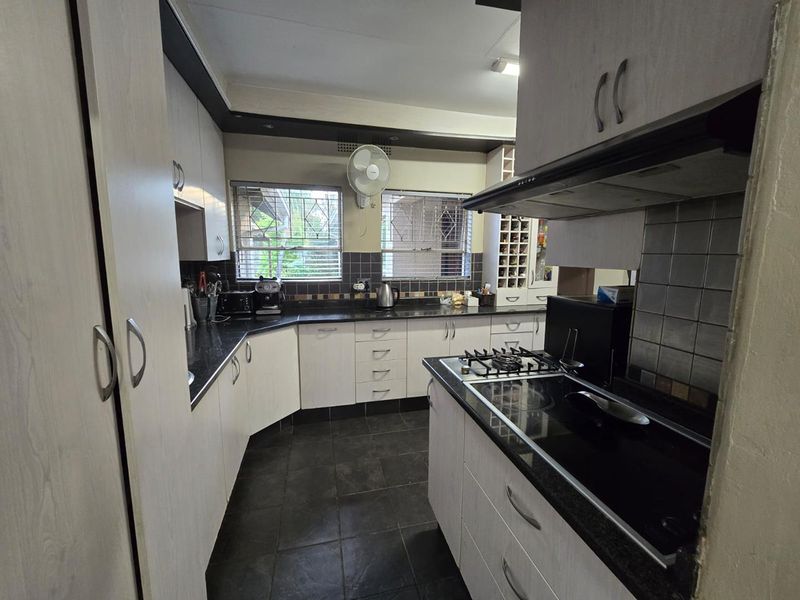 A functional kitchen featuring built-in cabinetry, granite countertops, a gas hob with extractor fan, and tiled flooring with security bars on the windows.