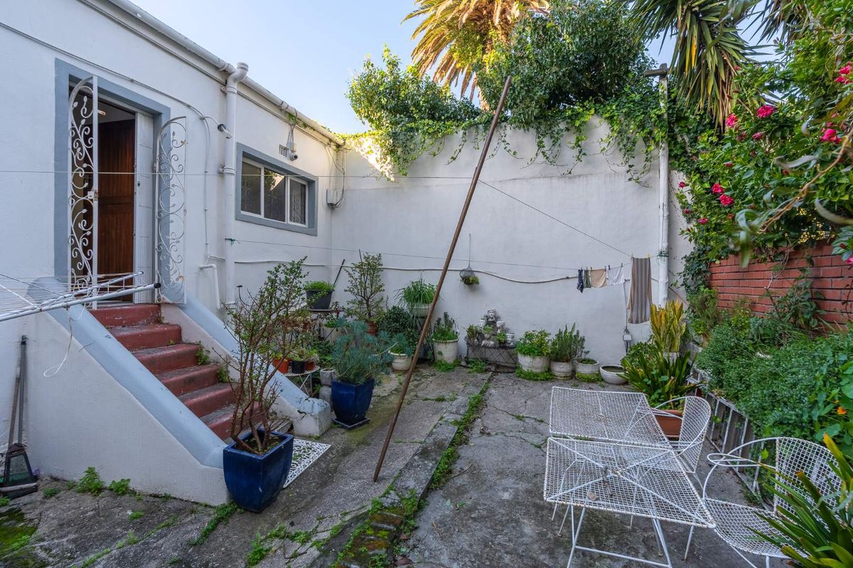 Rear courtyard area featuring a concrete patio, external staircase access, and perimeter boundary walls with established greenery.