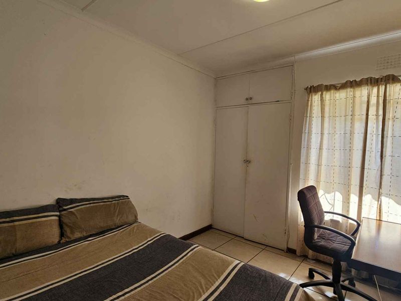 A bedroom featuring tiled flooring and built-in cupboards, offering a functional space that would benefit from cosmetic updates to the wall finishes.