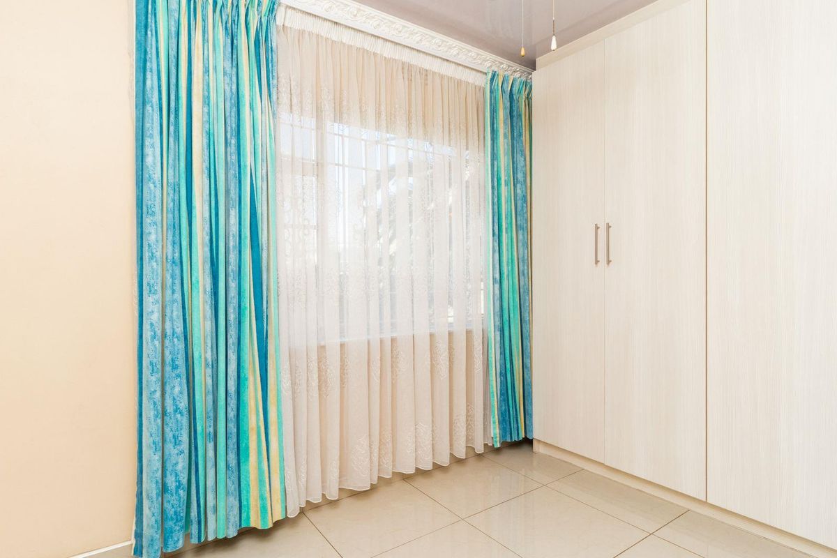 A bright bedroom featuring built-in floor-to-ceiling wardrobes, tiled flooring, and decorative ceiling cornicing.