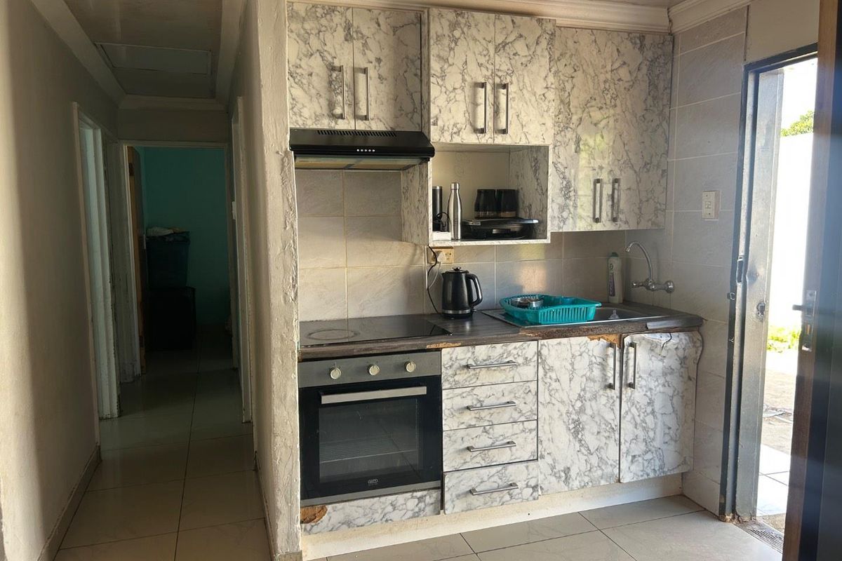 Compact kitchen featuring marble-effect cabinetry, built-in oven, electric hob, extractor fan, and tiled flooring with direct access to the exterior.