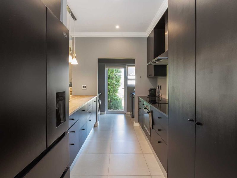 Modern galley-style kitchen featuring sleek dark cabinetry, timber countertops, integrated appliances, and tiled flooring with direct access to the exterior.