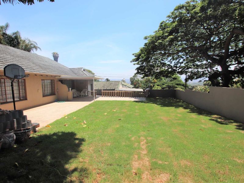 A spacious rear garden featuring a paved patio area, a well-maintained lawn, and a boundary wall with a balustrade overlooking the surrounding landscape.
