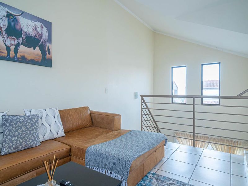 A bright living area featuring vaulted ceilings, tiled flooring, and a modern metal balustrade overlooking the lower level.