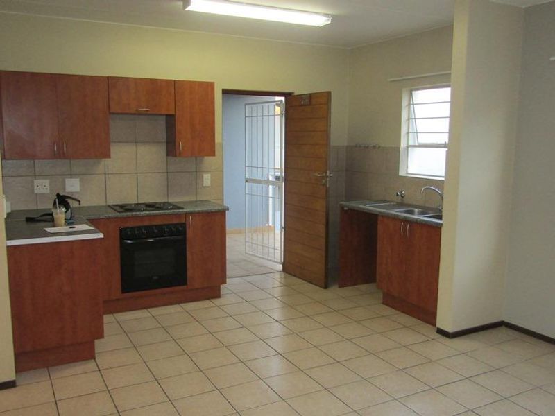 Open plan kitchen and living area featuring laminate cabinetry, built-in oven, electric hob, double sink, and tiled flooring throughout.