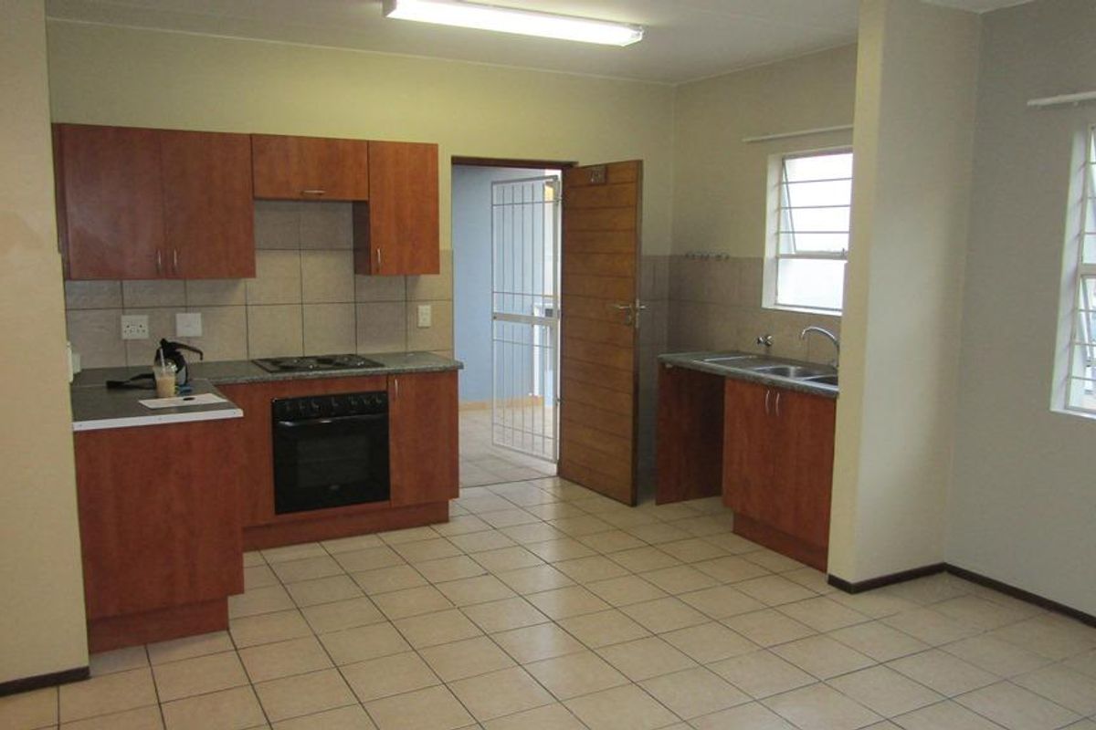 Open plan kitchen and living area featuring laminate cabinetry, built-in oven, electric hob, double sink, and tiled flooring throughout.
