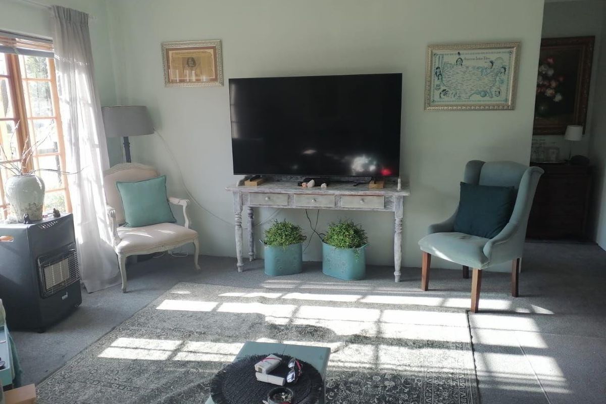 A comfortable living room featuring a large wall-mounted television, carpeted flooring, and natural light streaming through the window.